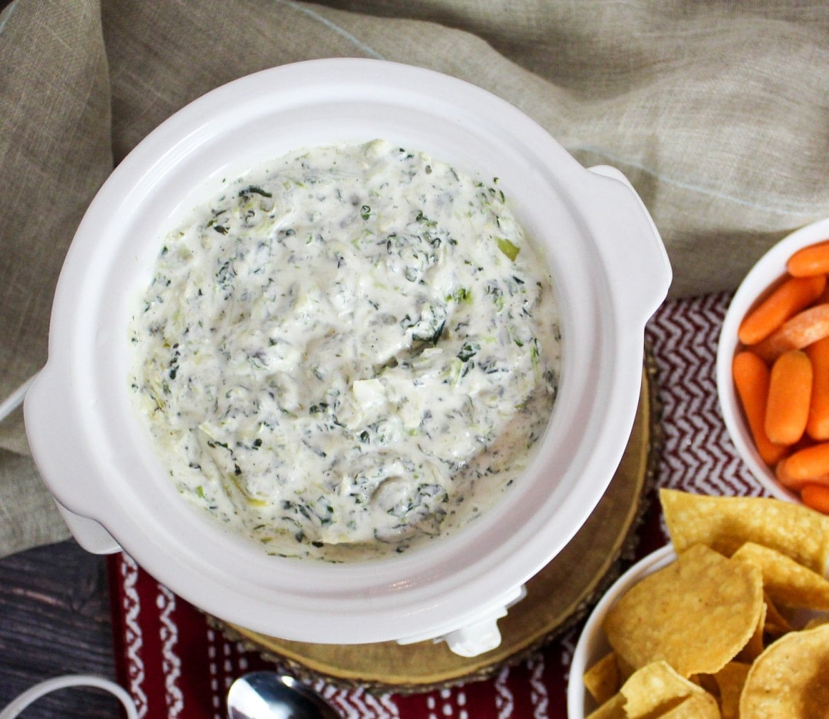 overhead picture of cheesy spinach and artichoke dip with chips and carrots