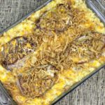 pork chops on top of cheesy potatoes in a casserole dish