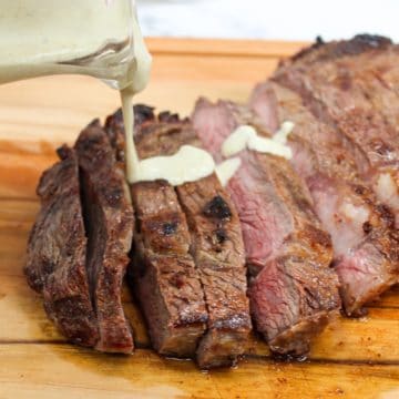 Grilled Ribeye with Garlic Blue Cheese Mustard Sauce on a cutting board and sliced with sauce on top