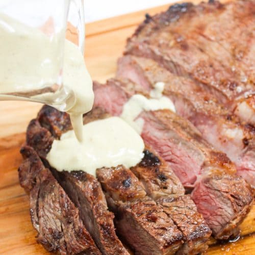 Grilled Ribeye with Garlic Blue Cheese Mustard Sauce on a cutting board and sliced with sauce on top