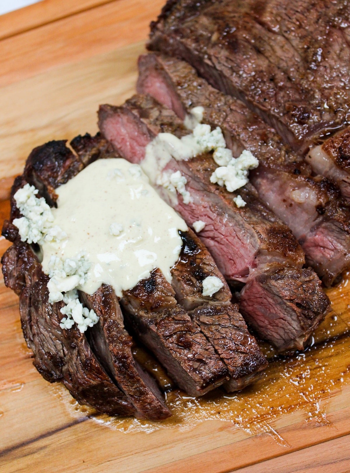 Grilled Ribeye with Garlic Blue Cheese Mustard Sauce on a cutting board and sliced with sauce on top