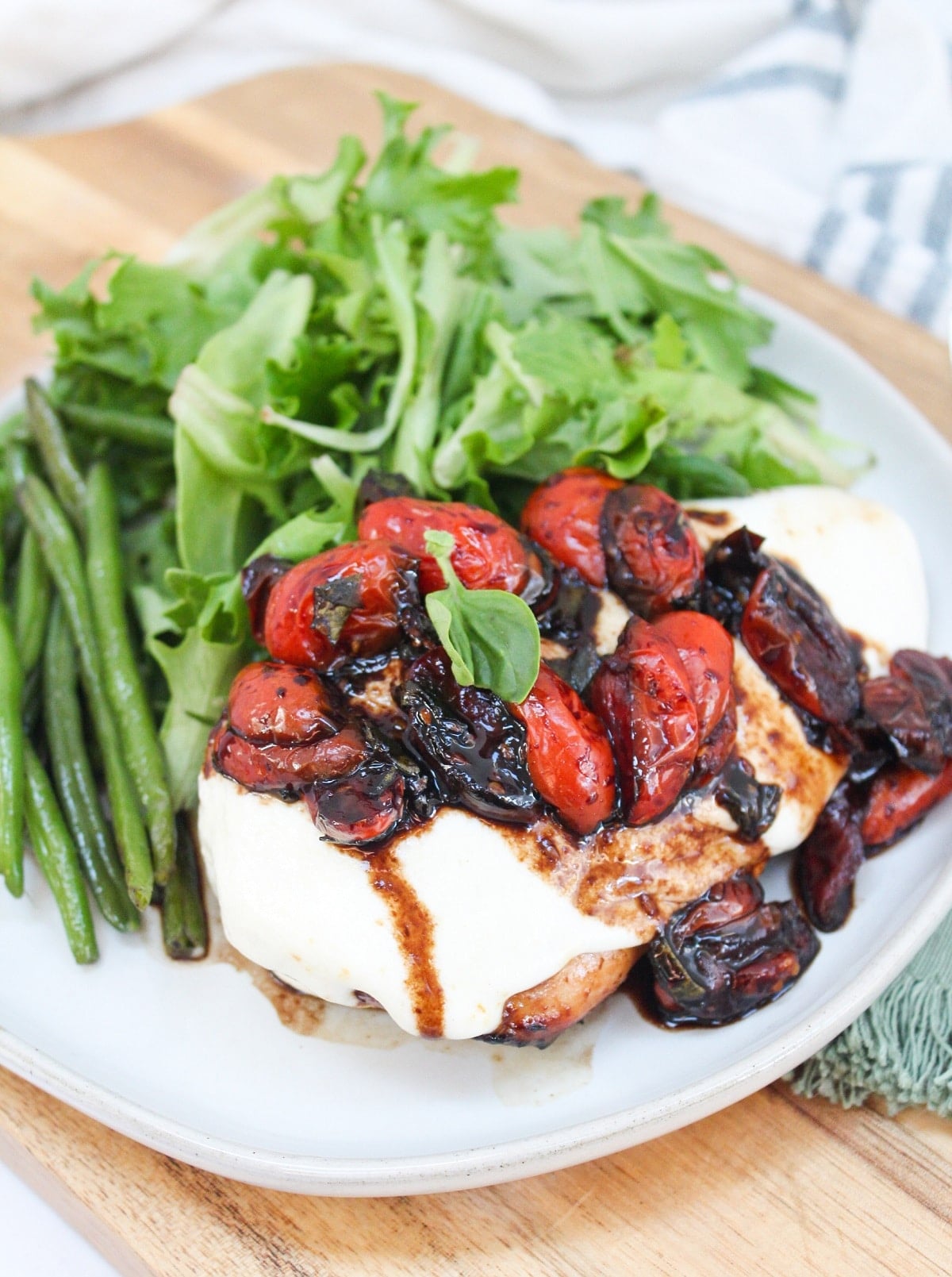 grilled caprese chicken plated with green beans and a salad.
