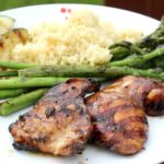 two grilled chicken thighs on a plate with grilled vegeetables