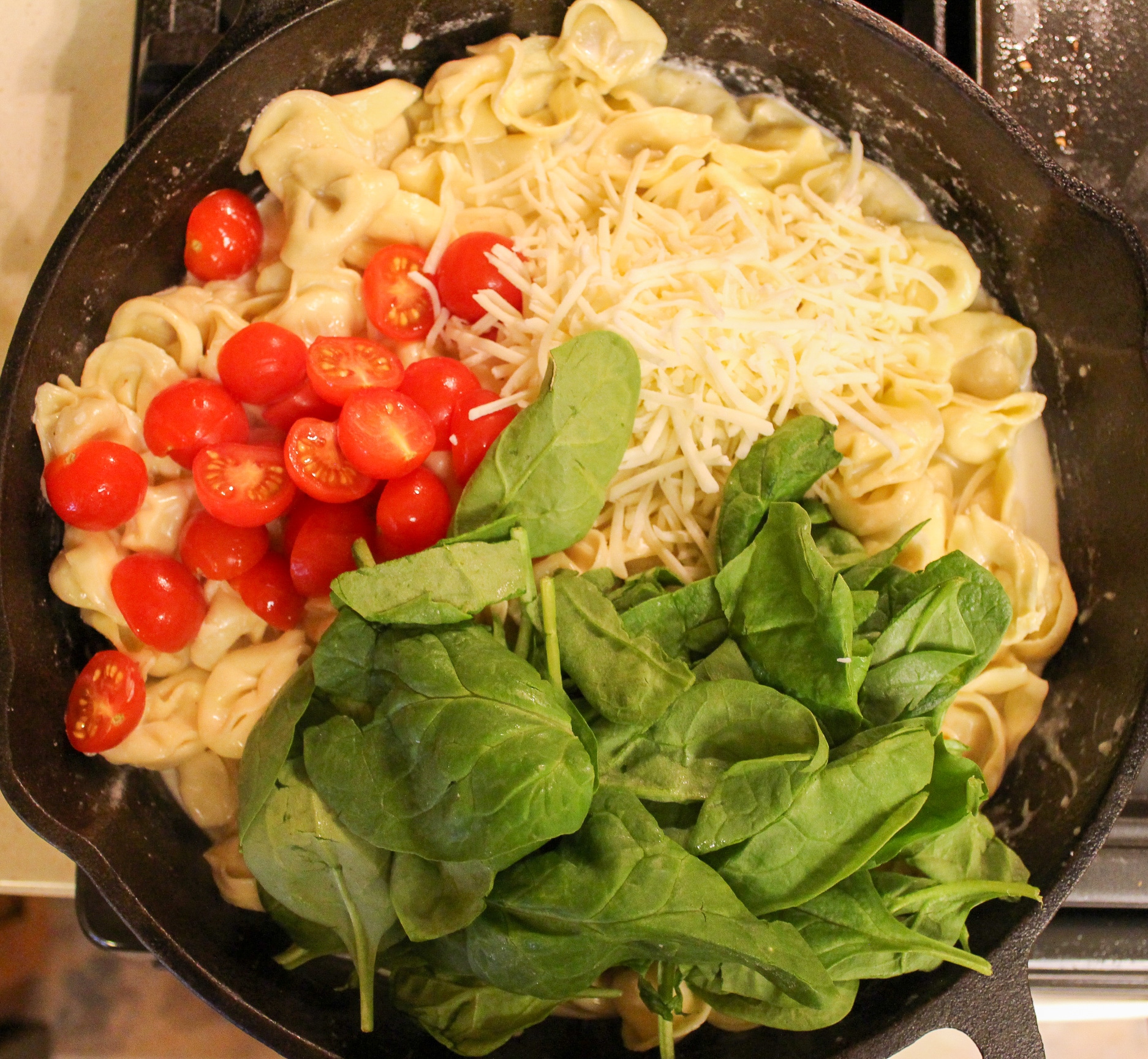 pasta in skillet with cheese, tomatoes, and spinach