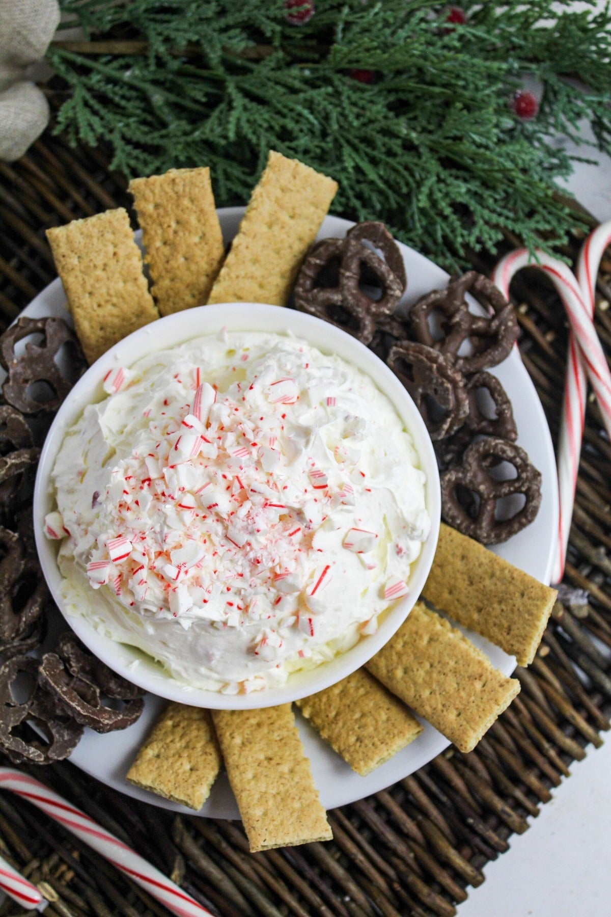 creamy white dip in a white bowl topped with crushed candy canes and surrounded by chocolate covered pretzels.