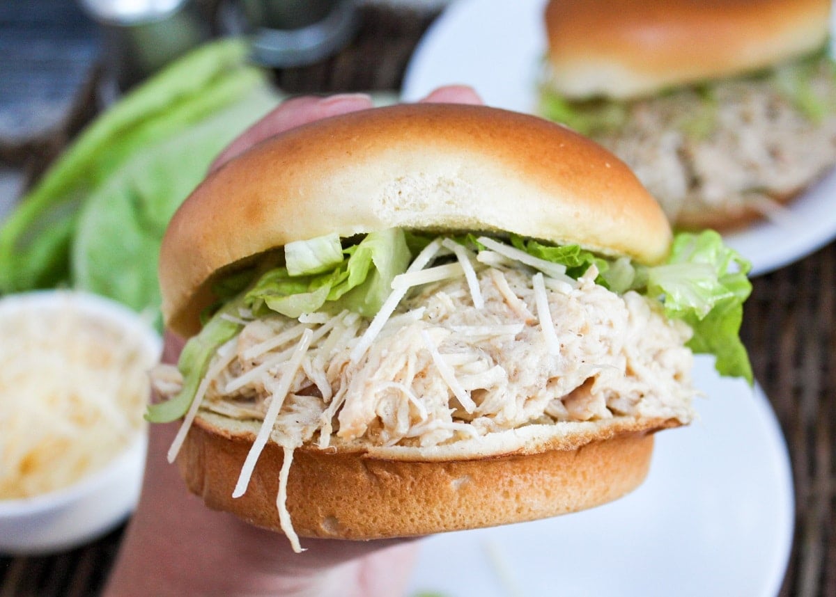 chicken on a bun with lettuce and cheese held in hand