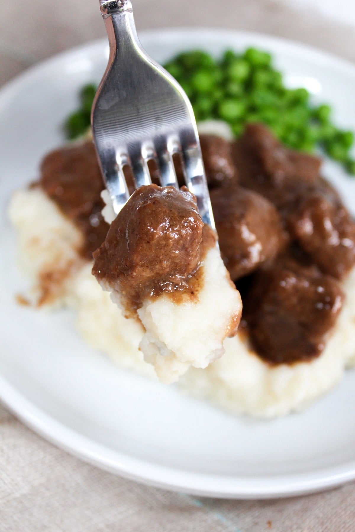 no peek beef tips on a plate with mashed potatoes and peas on a fork