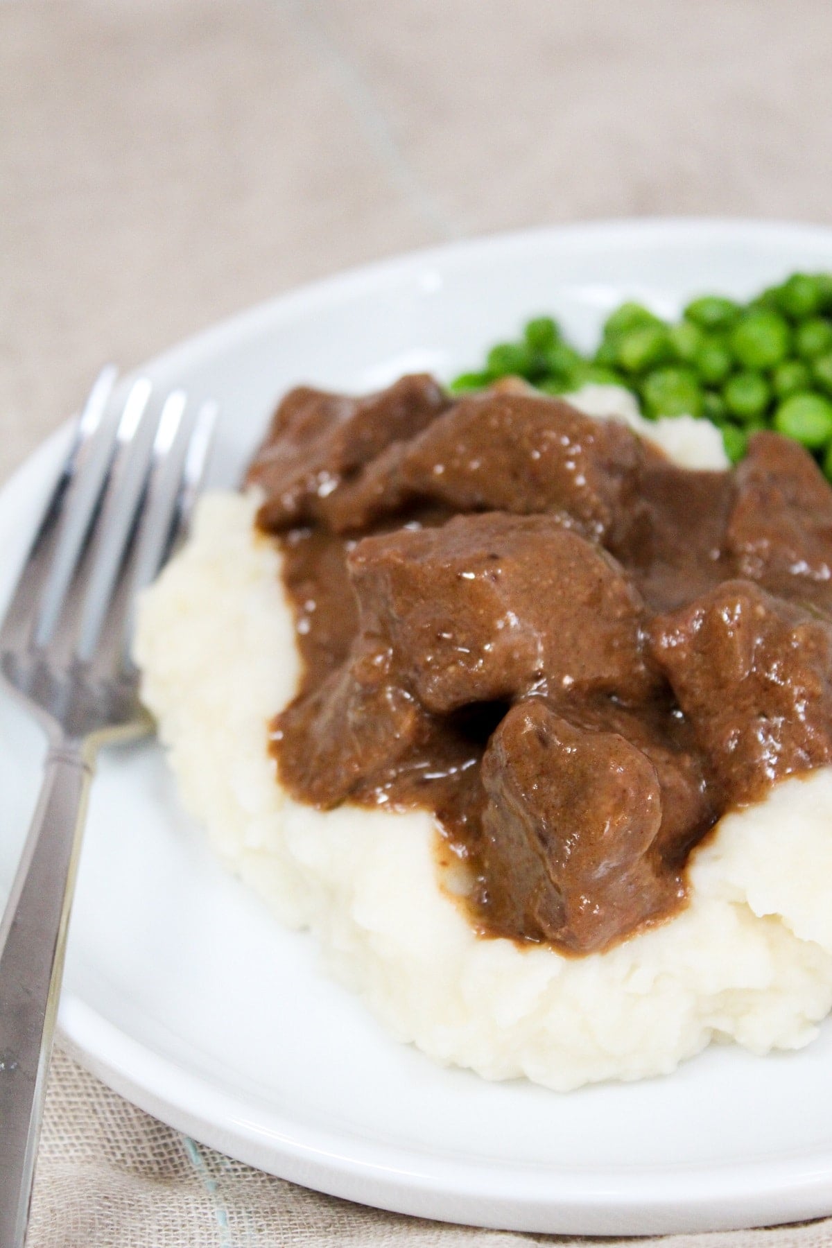 no peek beef tips on a plate with mashed potatoes and peas