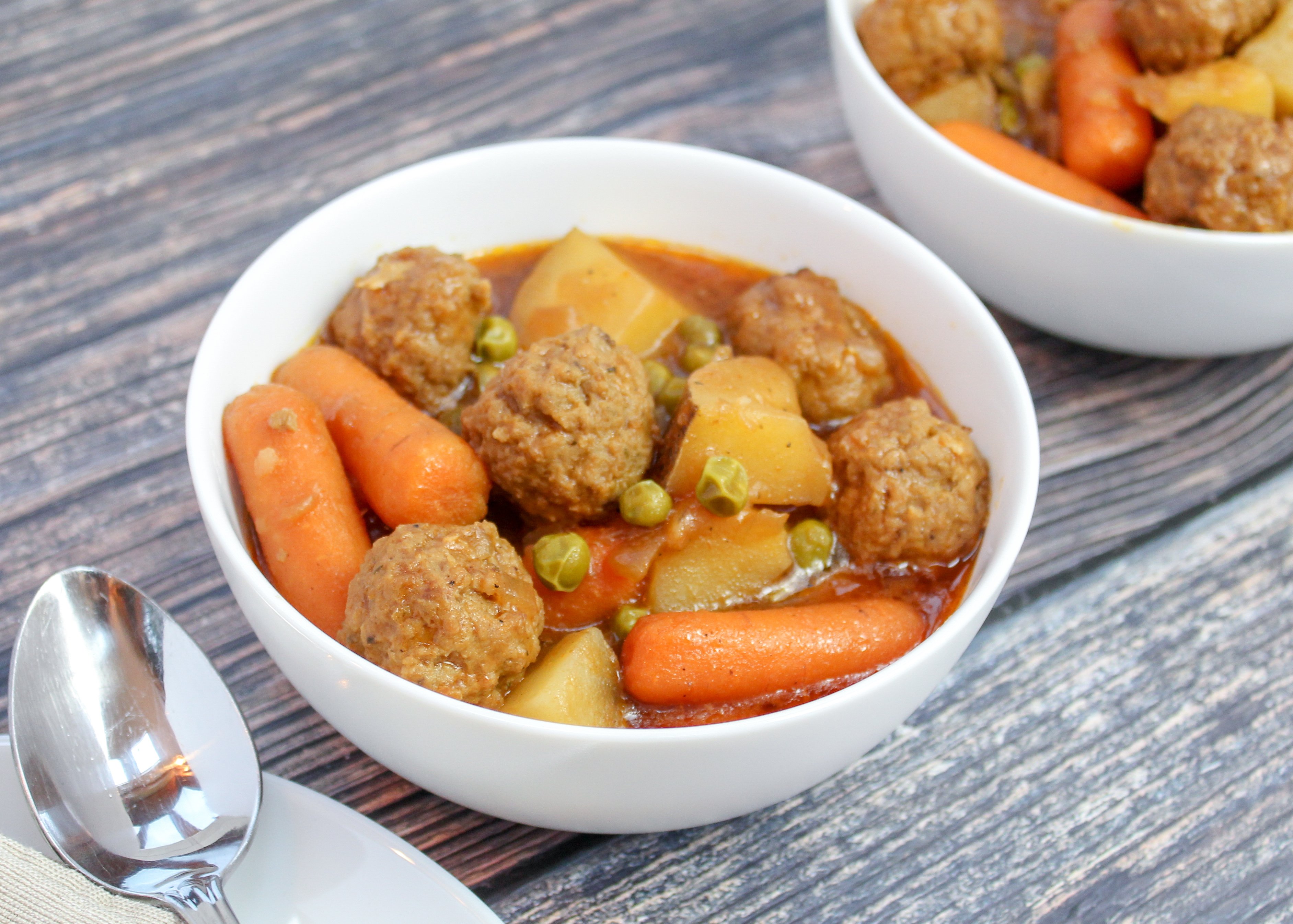 White bowl filled with meatballs, carrots, celery, potatoes and peas