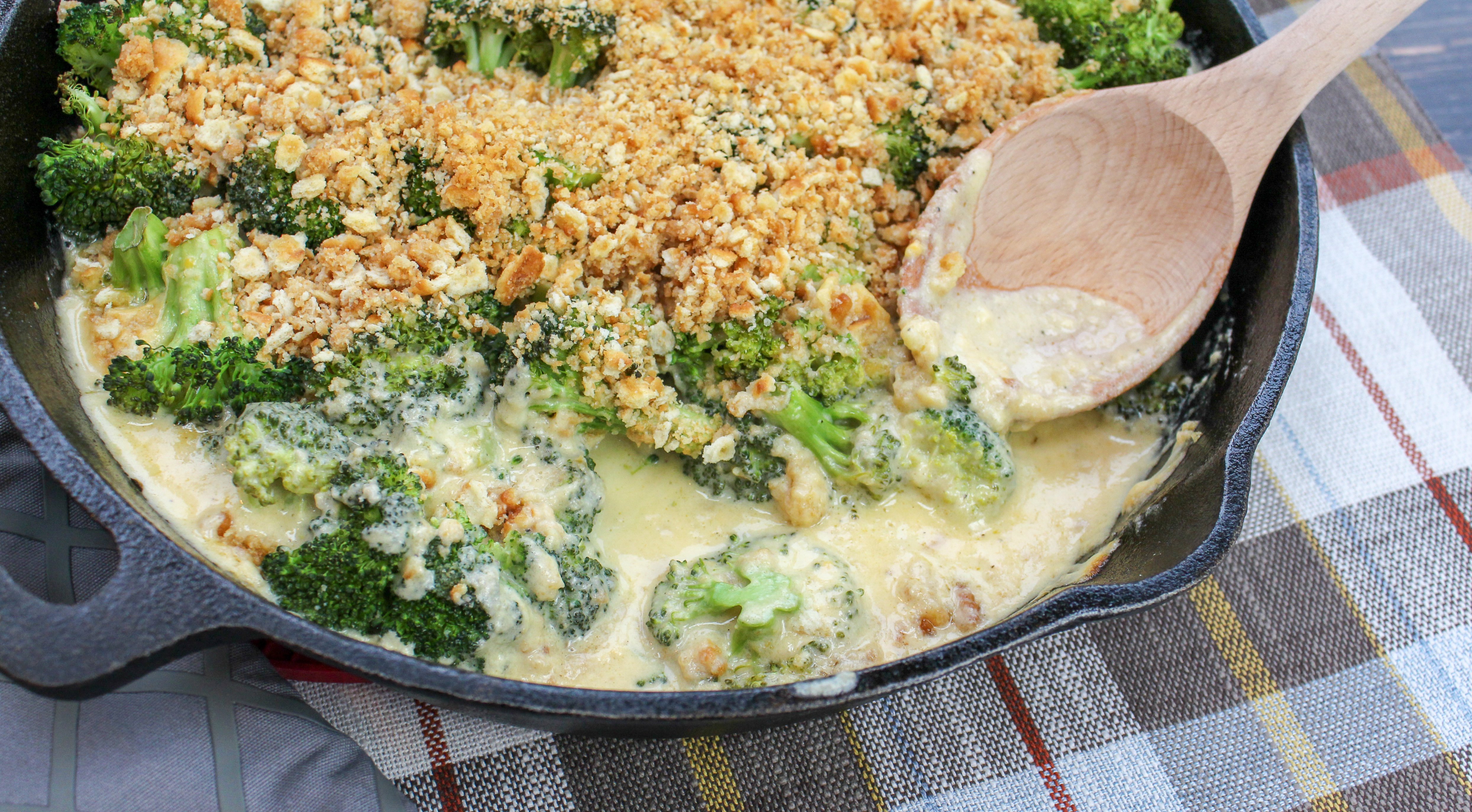 Broccoli florets covered in cheese sauce and topped with crushed crackers. Served in a round black baking pan.
