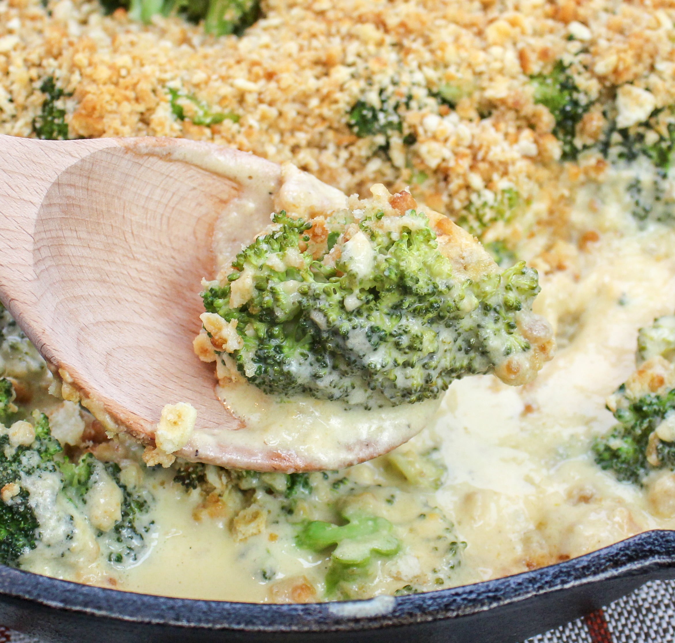 Broccoli florets covered in cheese sauce and topped with crushed crackers. Served in a round black baking pan.