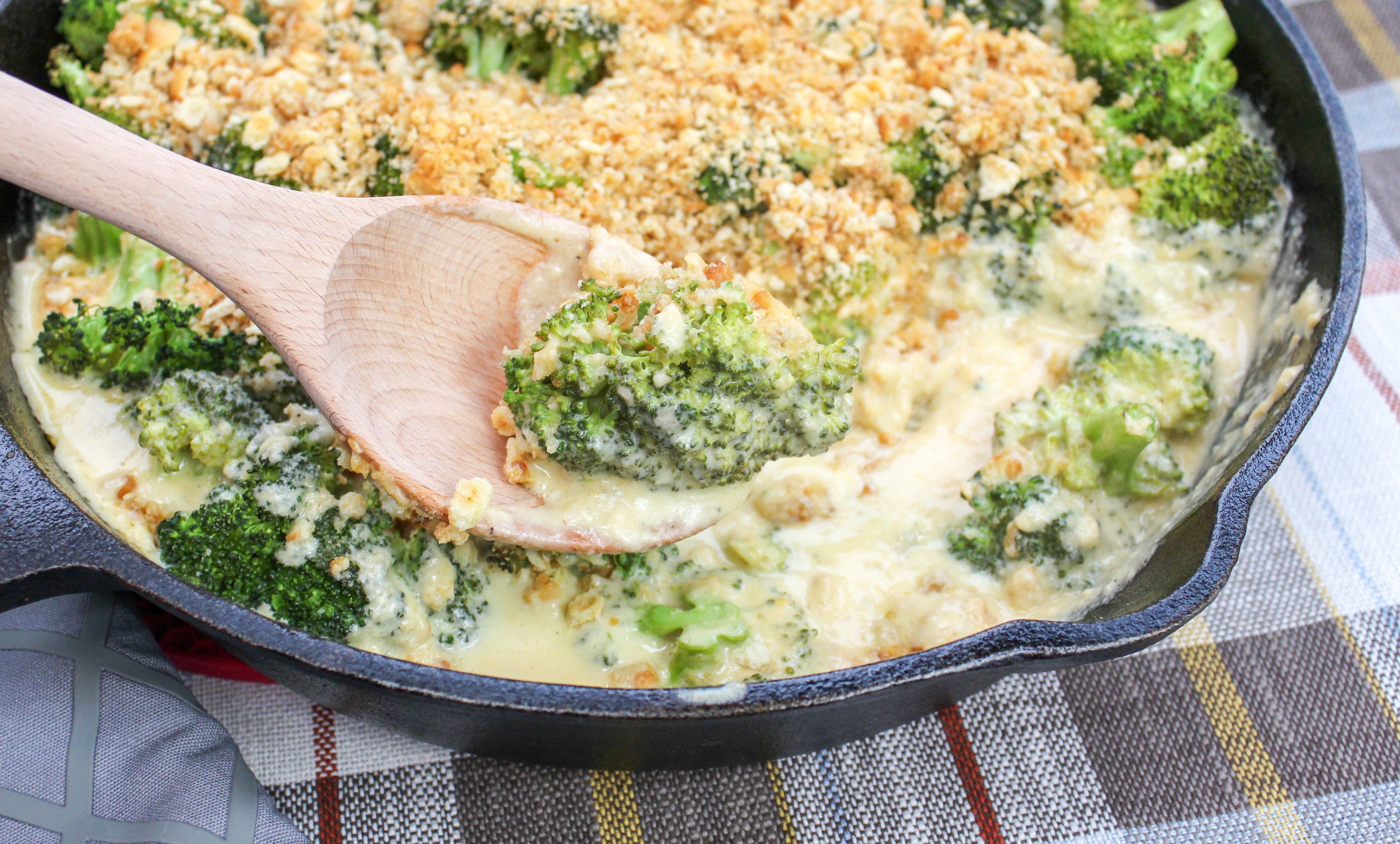 Broccoli florets covered in cheese sauce and topped with crushed crackers. Served in a round black baking pan.
