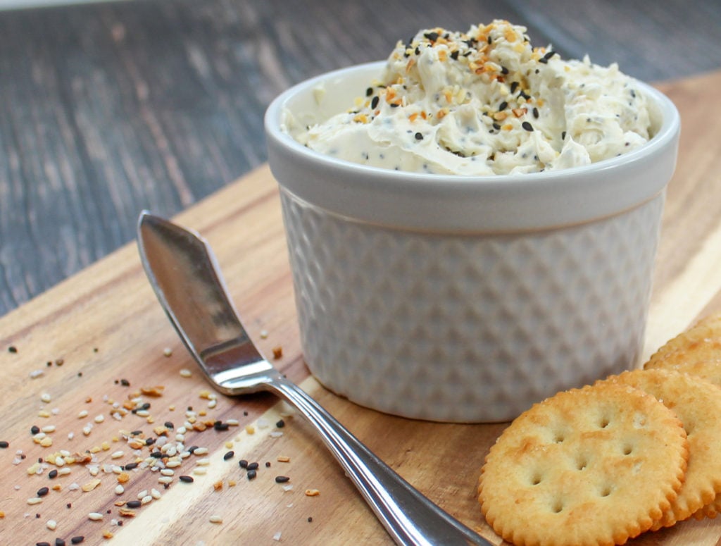 Spread in a white container wth crackers and a spreading knife