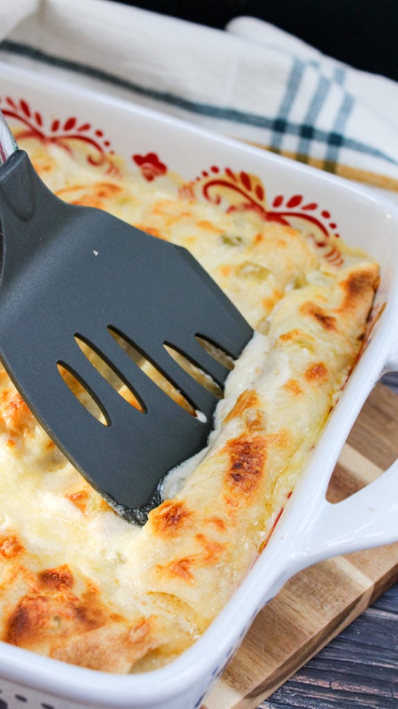 Chicken enchiladas in a baking dish with a spatula