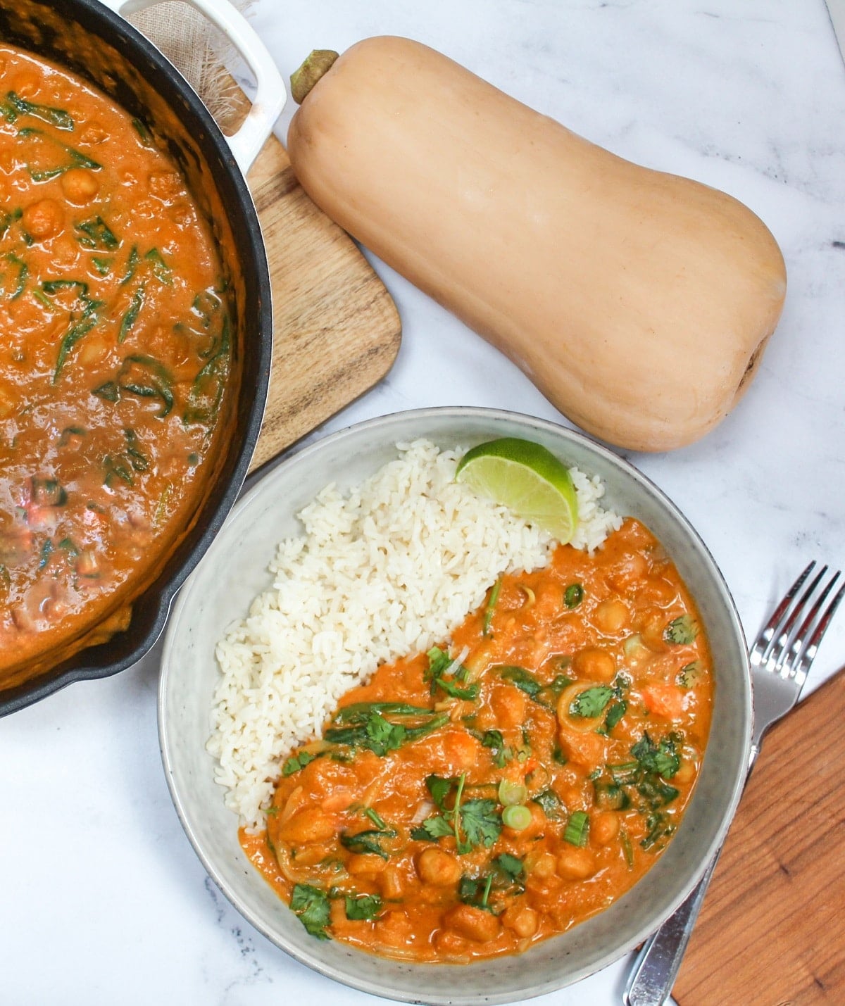 thai butternut squash curry in a bowl with rice next to a skillet with more curry