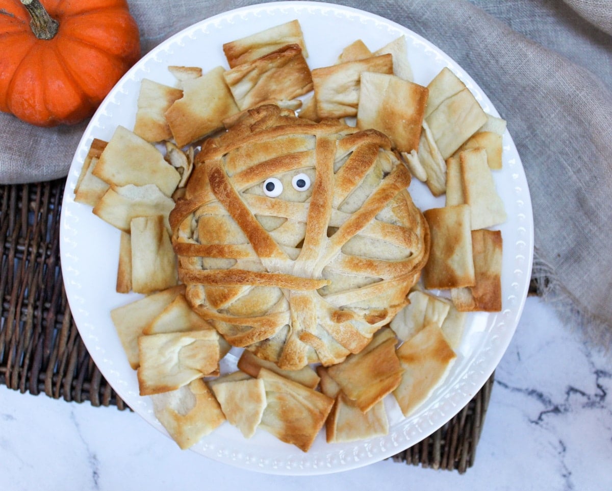 mummy wrapped brie on a plate with crackers