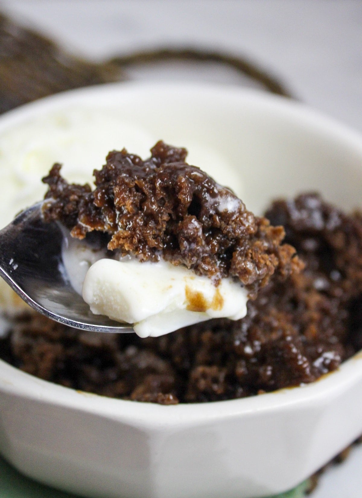 slow cooker chocolate cobbler in a bowl with vanilla ice cream with spoon