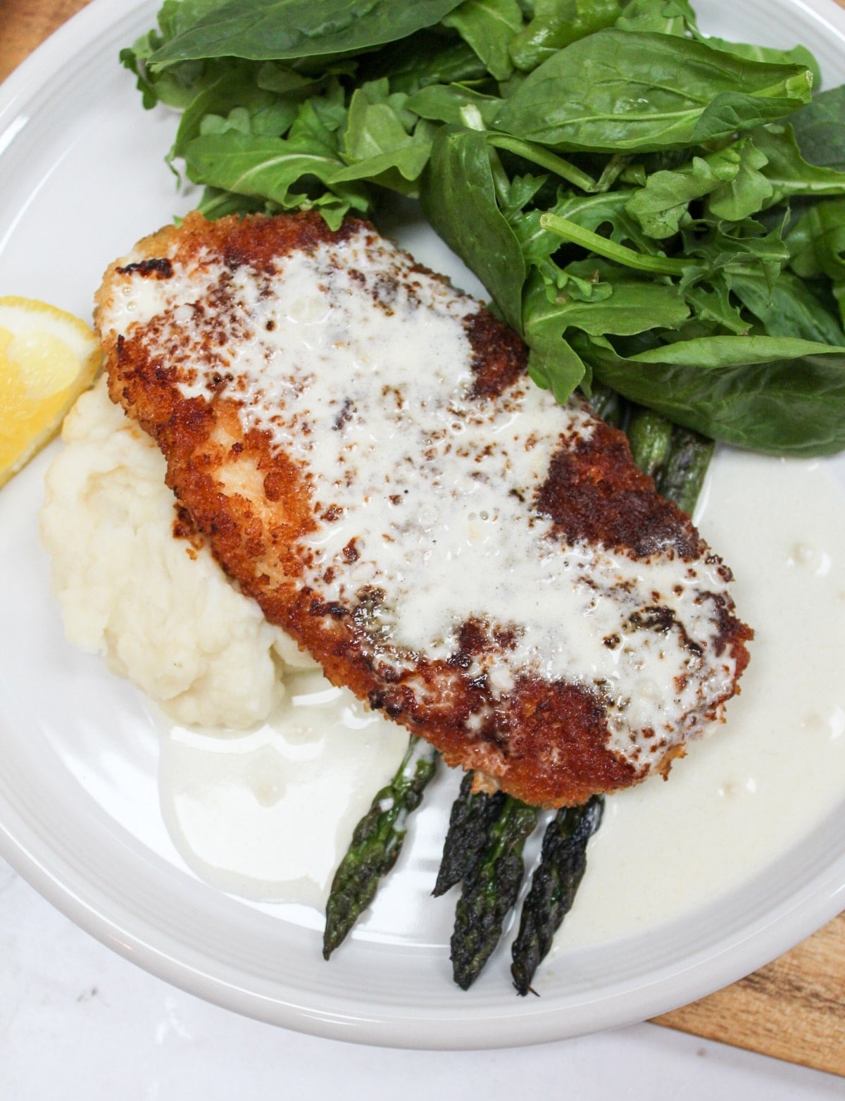 chicken costoletta on a plate with lemon sauce and asparagus.