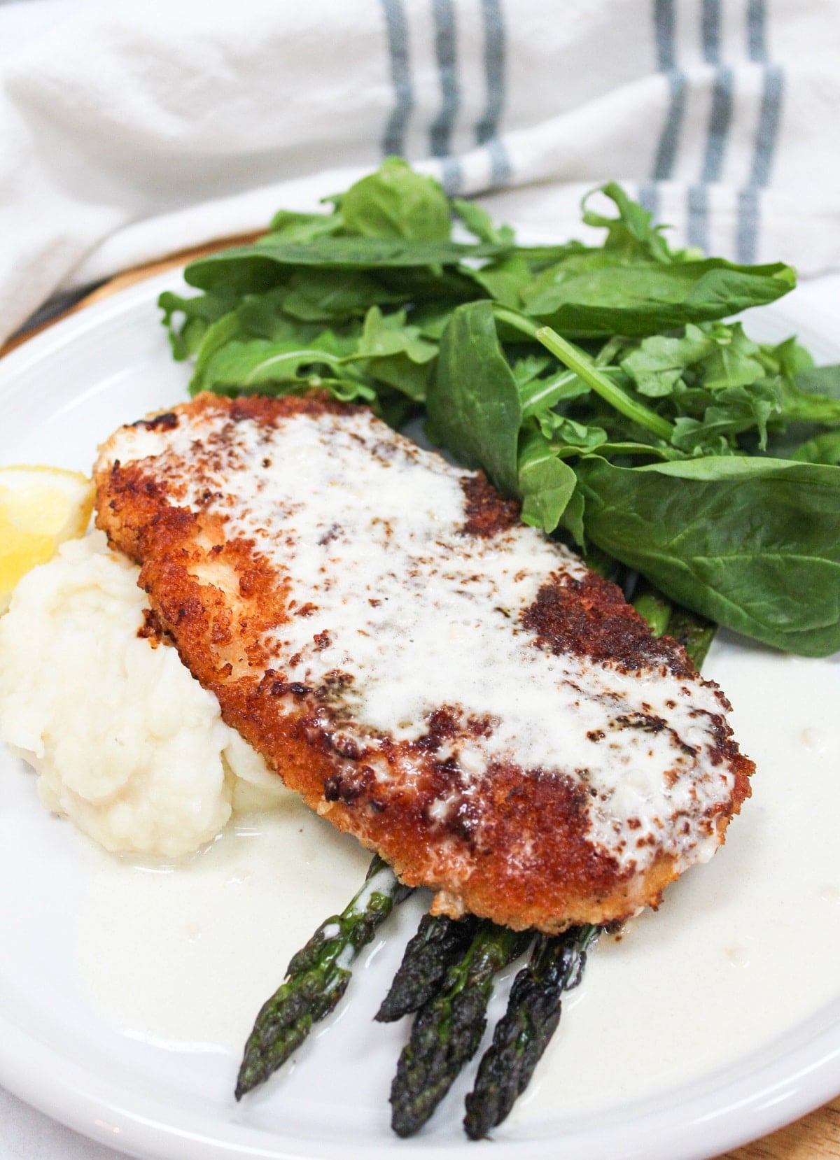 chicken costoletta on a plate with lemon sauce and asparagus.