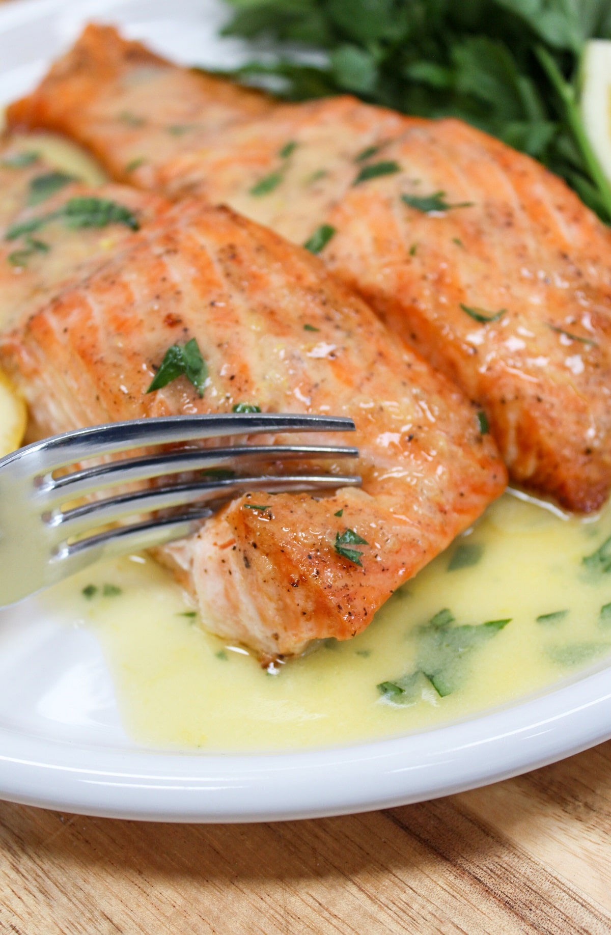 salmon on a white plate with lemons with sauce poured over the top cut with a fork.