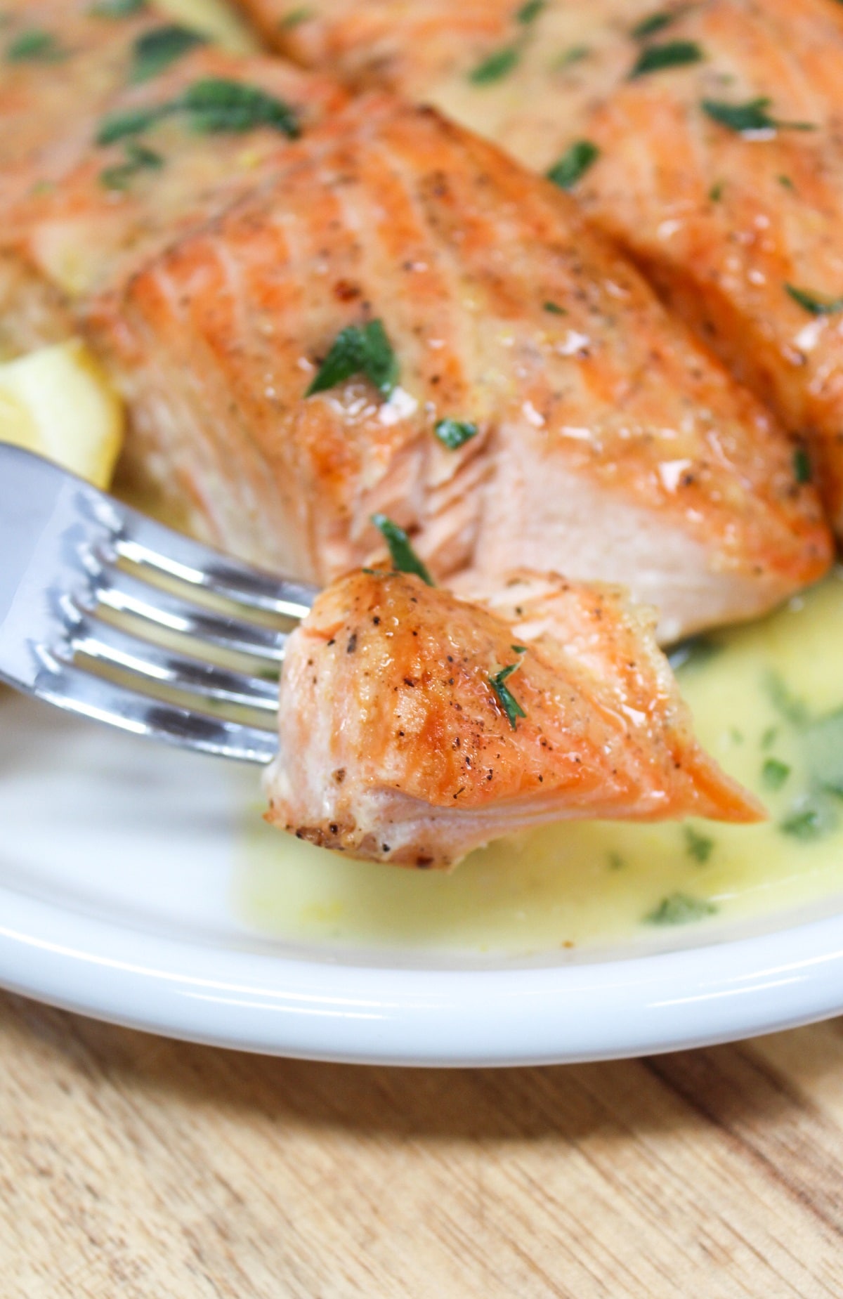 salmon on a white plate with lemons with sauce poured over the top cut with a fork.