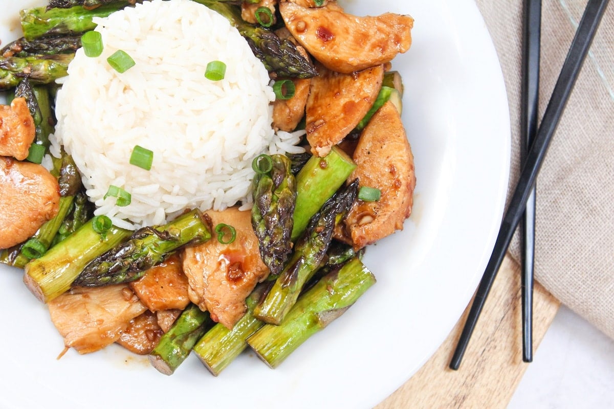 chicken and asparagus stir fry in a bowl with rice.
