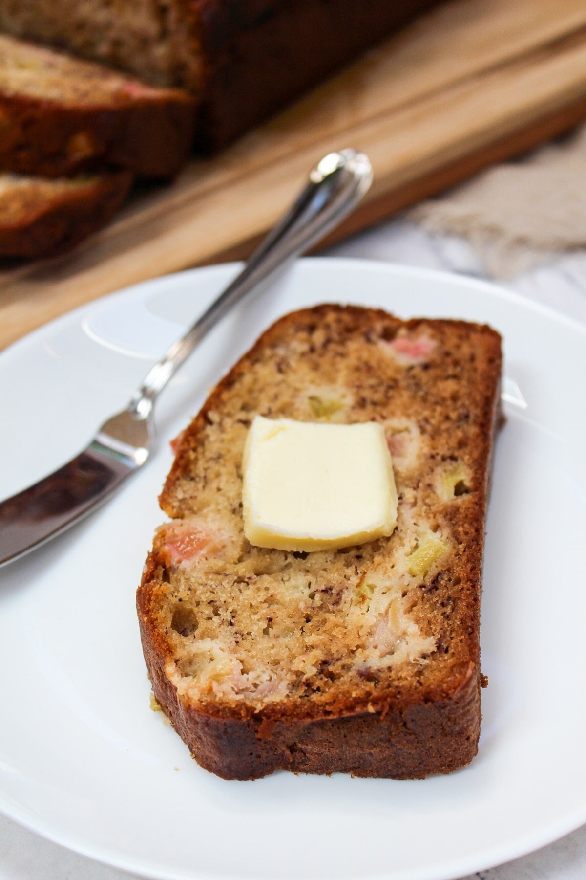 Sliced Rhubarb Banana bread on a white plate with butter.