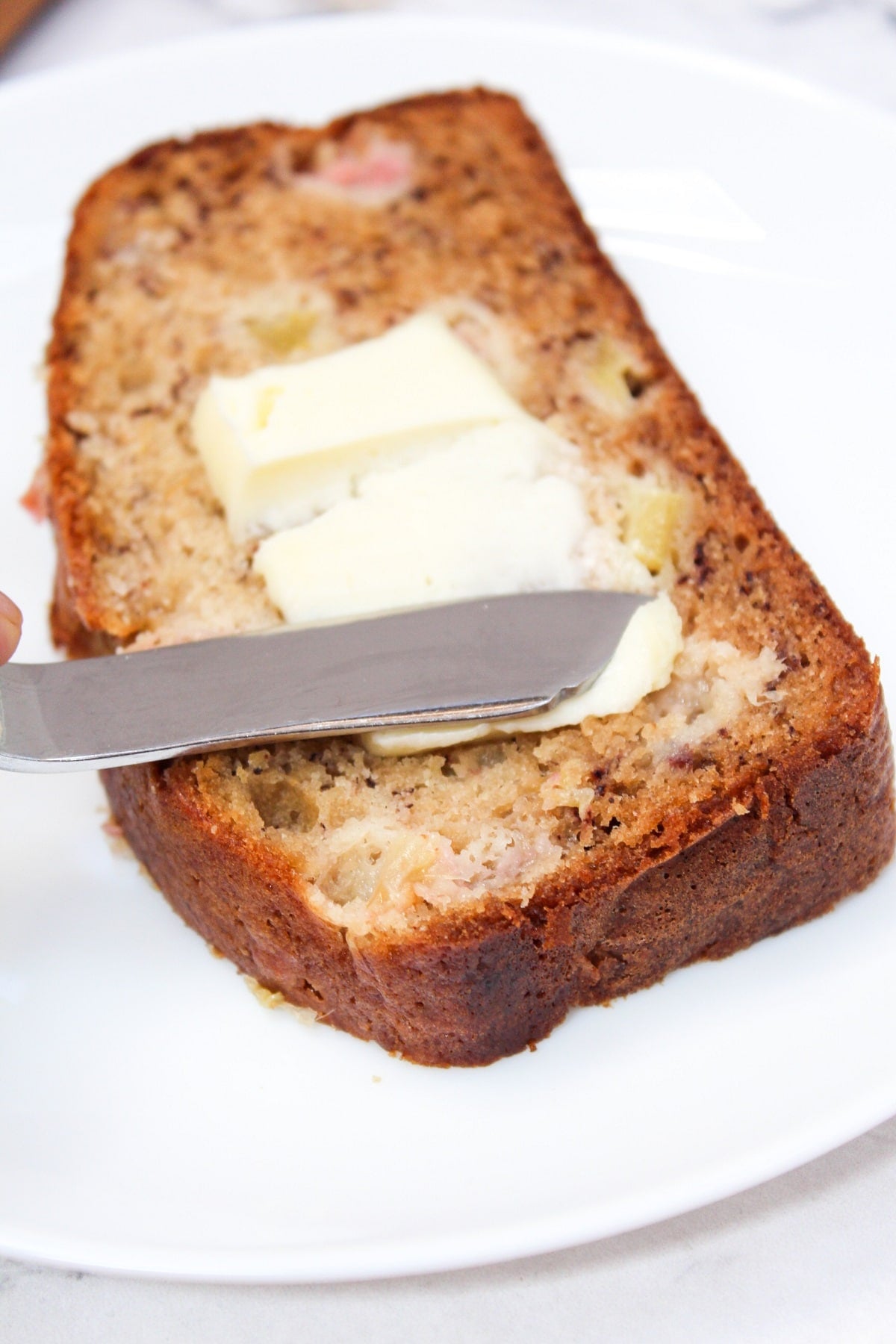 Sliced Rhubarb Banana bread on a white plate with butter.