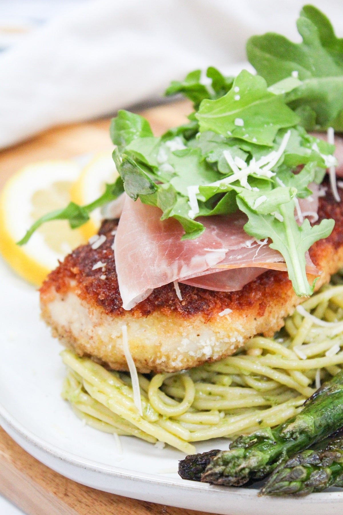 chicken bellagio over pasta topped with arugula and served wit asparagus.