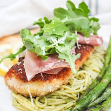 chicken bellagio over pasta topped with arugula and served wit asparagus.