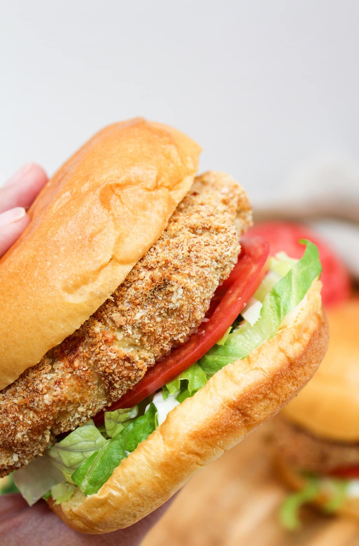 crispy chicken patty on a bun with shredded lettuce and sliced tomato held in hand.
