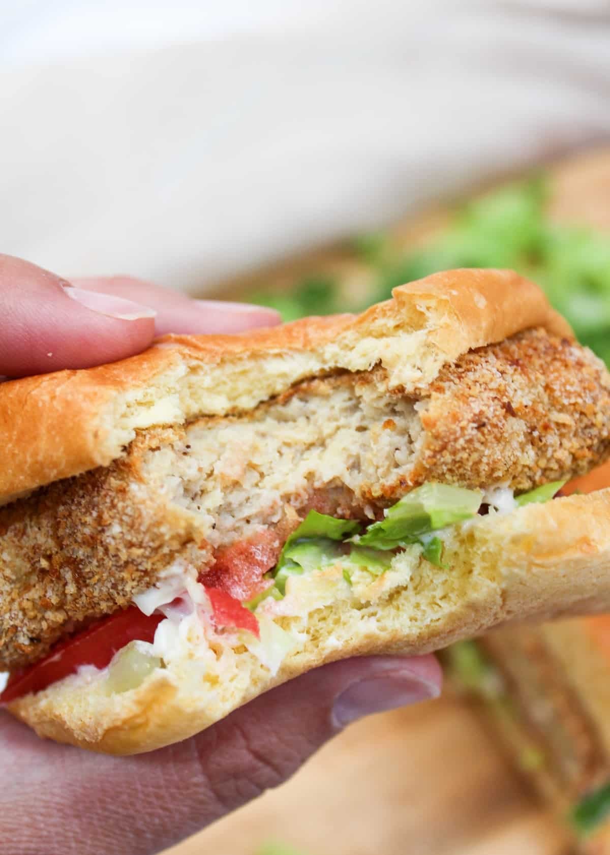crispy chicken patty on a bun with shredded lettuce and sliced tomato with a bite taken.