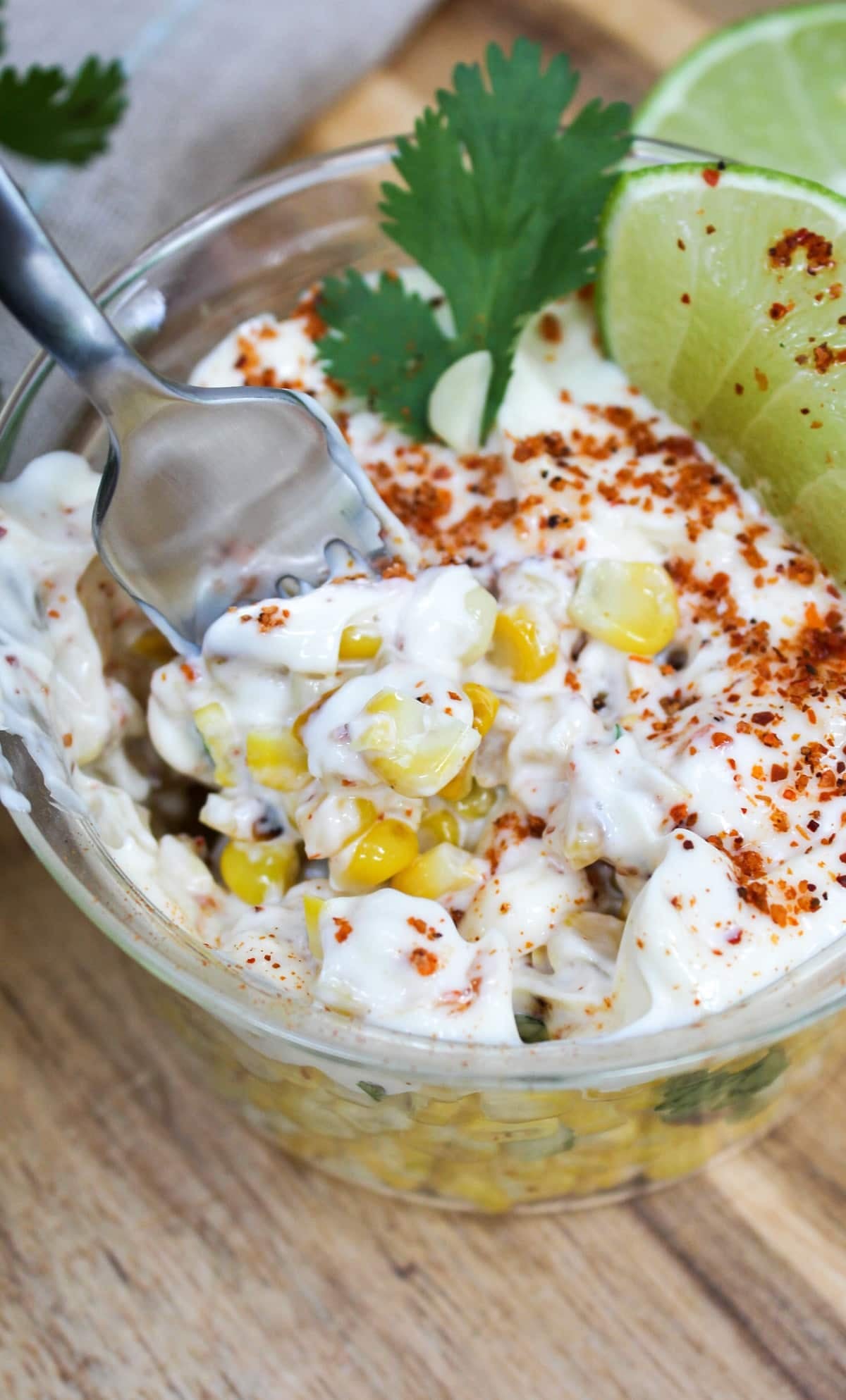 Mexican Street Corn Elote Bowl in a glass dish with lime and cilantro on top. The bowl is mixed together with a fork.
