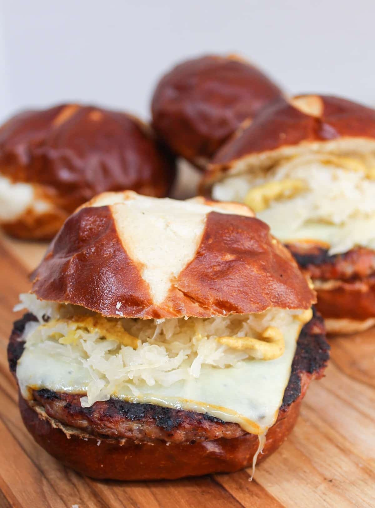 grilled brat pattie on a pretzel roll. The meat is cooked and topped with melted cheese, mustard, and sauerkraut.