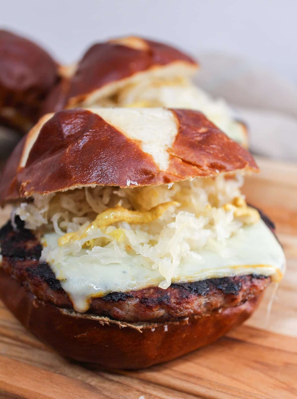 grilled brat pattie on a pretzel roll. The meat is cooked and topped with melted cheese, mustard, and sauerkraut.