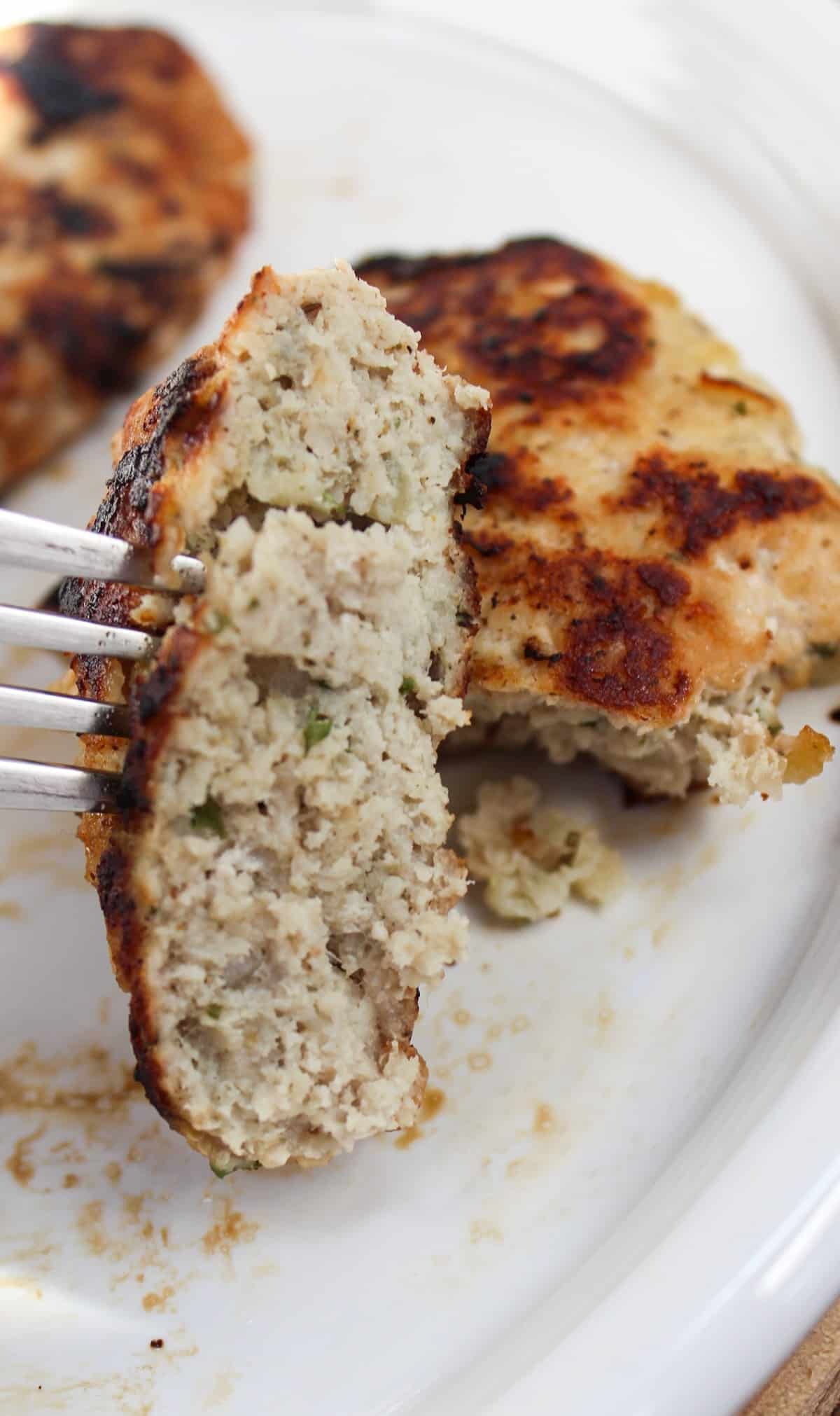 chicken formed into sausage patties. Cooked in a skillet till golden brown and served on a white plate and cut with a fork.