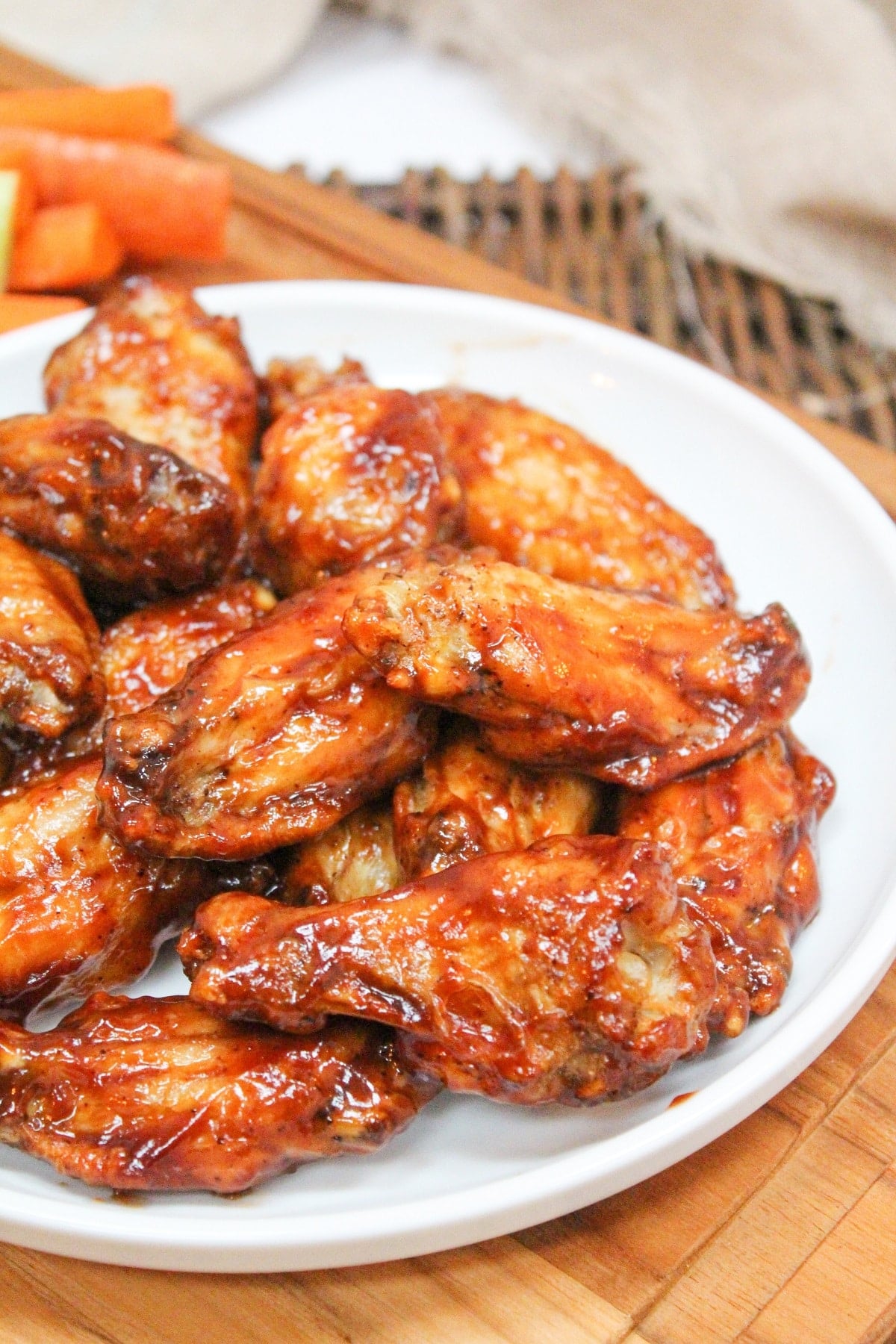 cooked wings in bbq sauce piled on a white plate. Sliced carrots and celery on the side with ranch dressing.