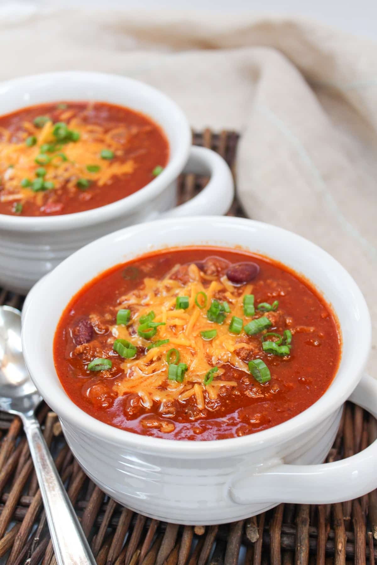 chili served in a white bowl. Topped with shredded cheddar cheese and sliced green onions.