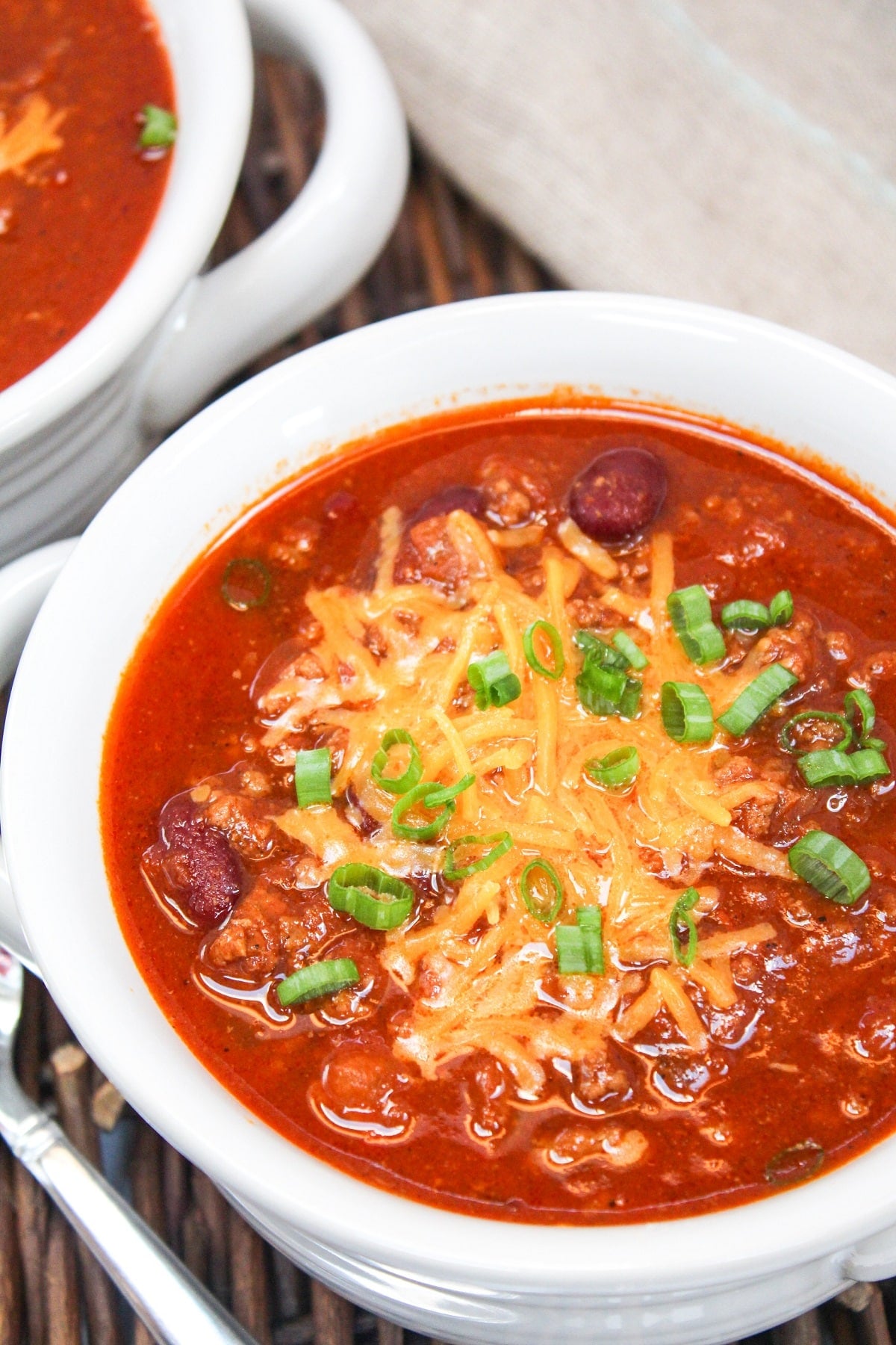 chili served in a white bowl. Topped with shredded cheddar cheese and sliced green onions.