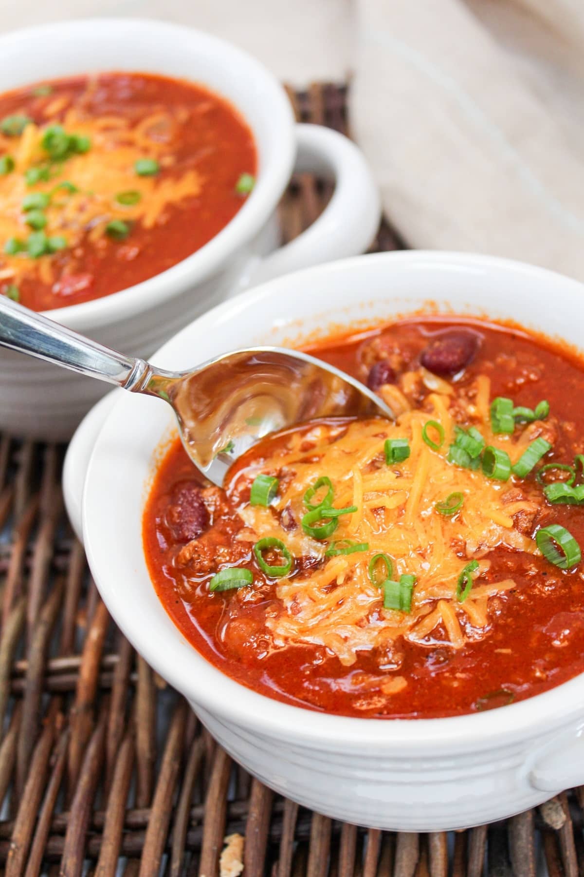 chili served in a white bowl. Topped with shredded cheddar cheese and sliced green onions.