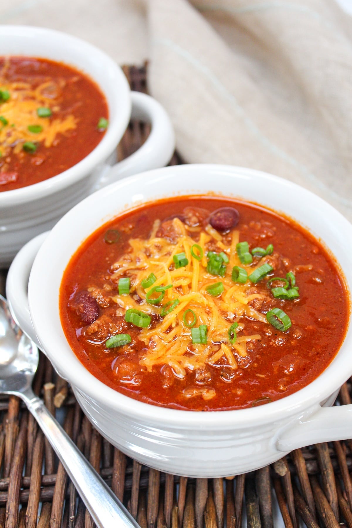 chili served in a white bowl. Topped with shredded cheddar cheese and sliced green onions.