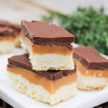 Cookie style bars cut into rectangles. The bars are layers wit h shortbread on the bottom, then caramel, and chocolate on top. The bars are stacked on top of each other.