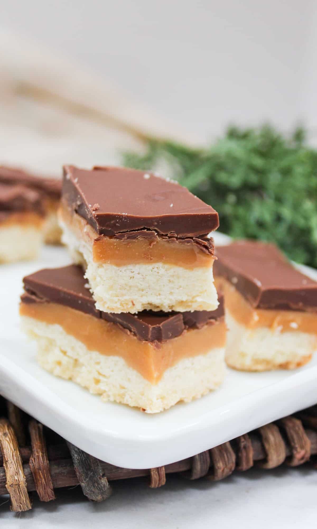 Cookie style bars cut into rectangles. The bars are layers wit h shortbread on the bottom, then caramel, and chocolate on top. The bars are stacked on top of each other.