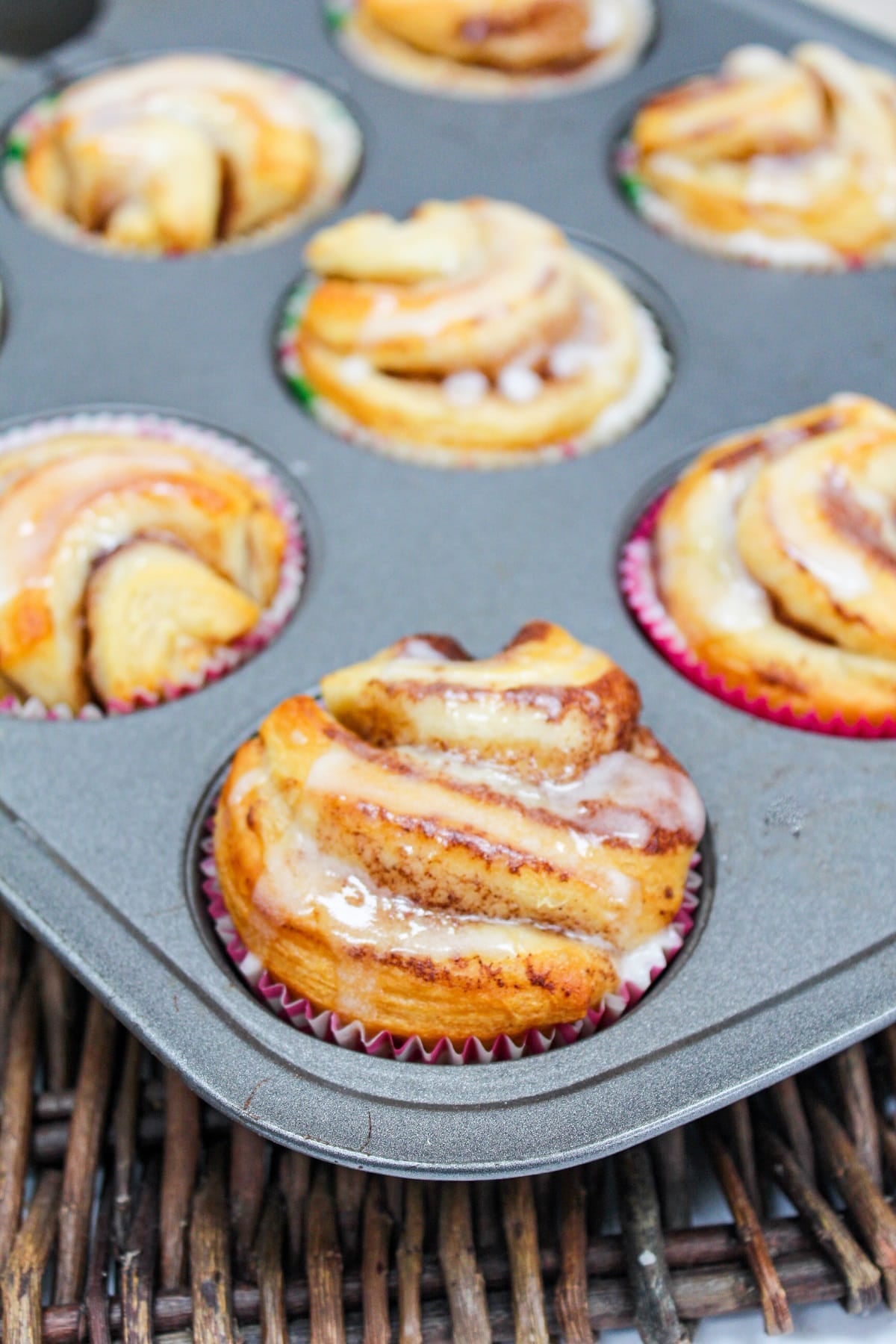 individual cinnamon rolls in a muffin tin with a glaze on top.