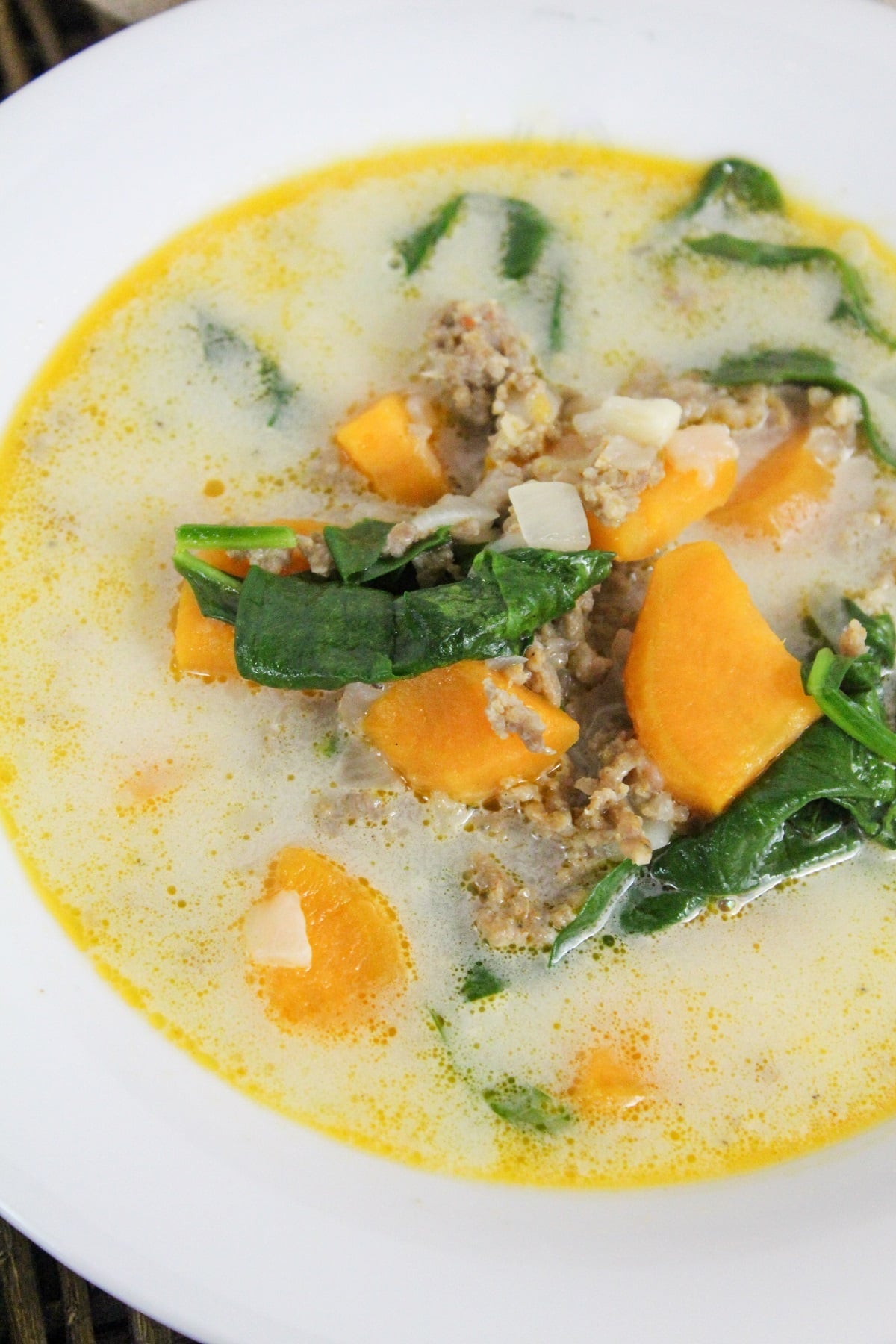 soup filled with sweet potatoes, ground sausage, and spinach in a white bowl.