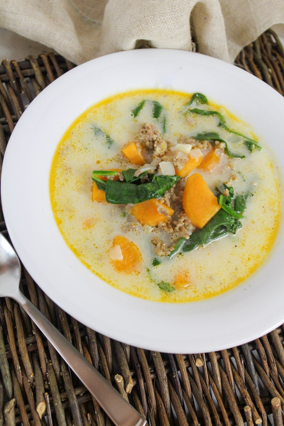 soup filled with sweet potatoes, ground sausage, and spinach in a white bowl.