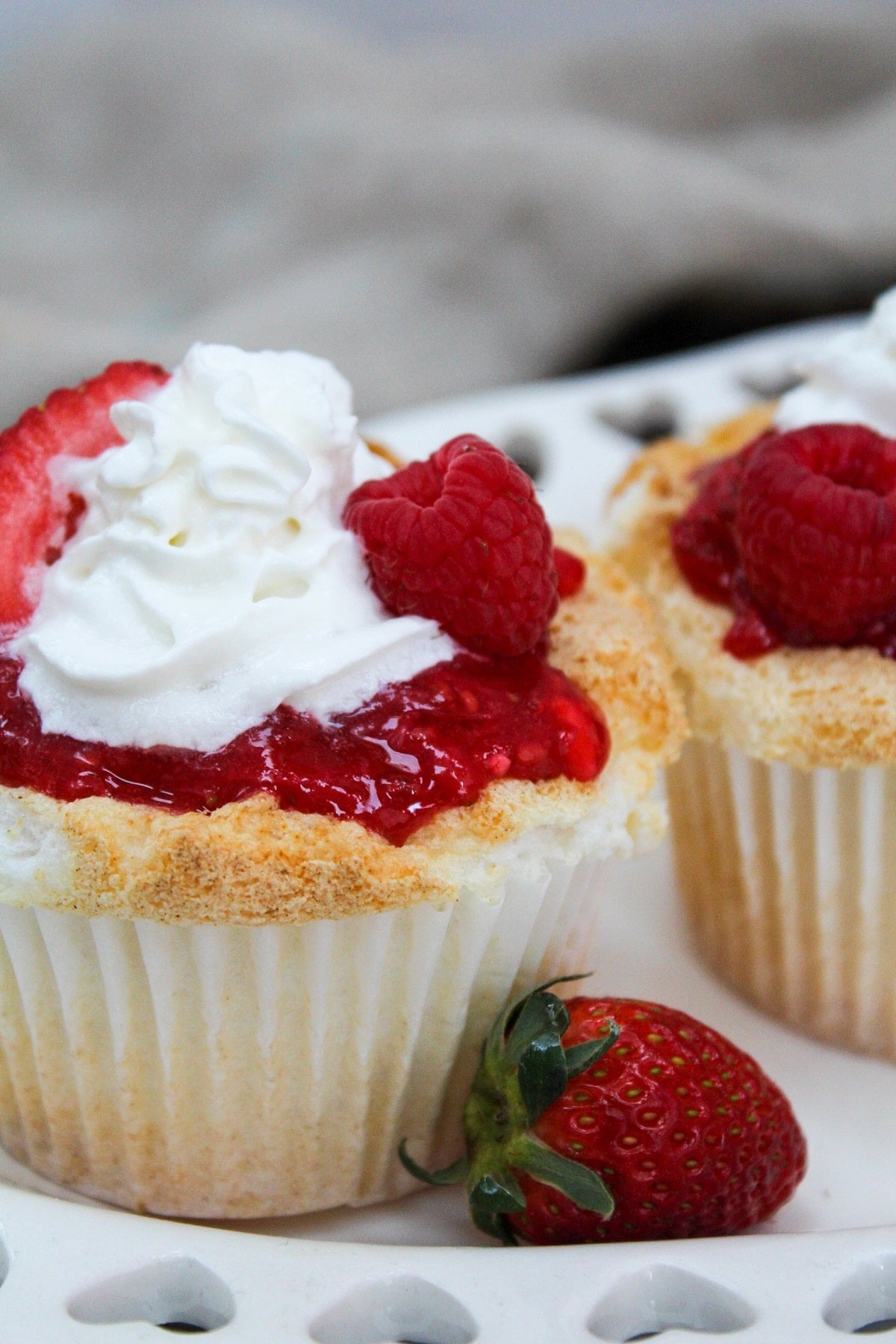 cupcake on a white plate with a strawberry on the side.