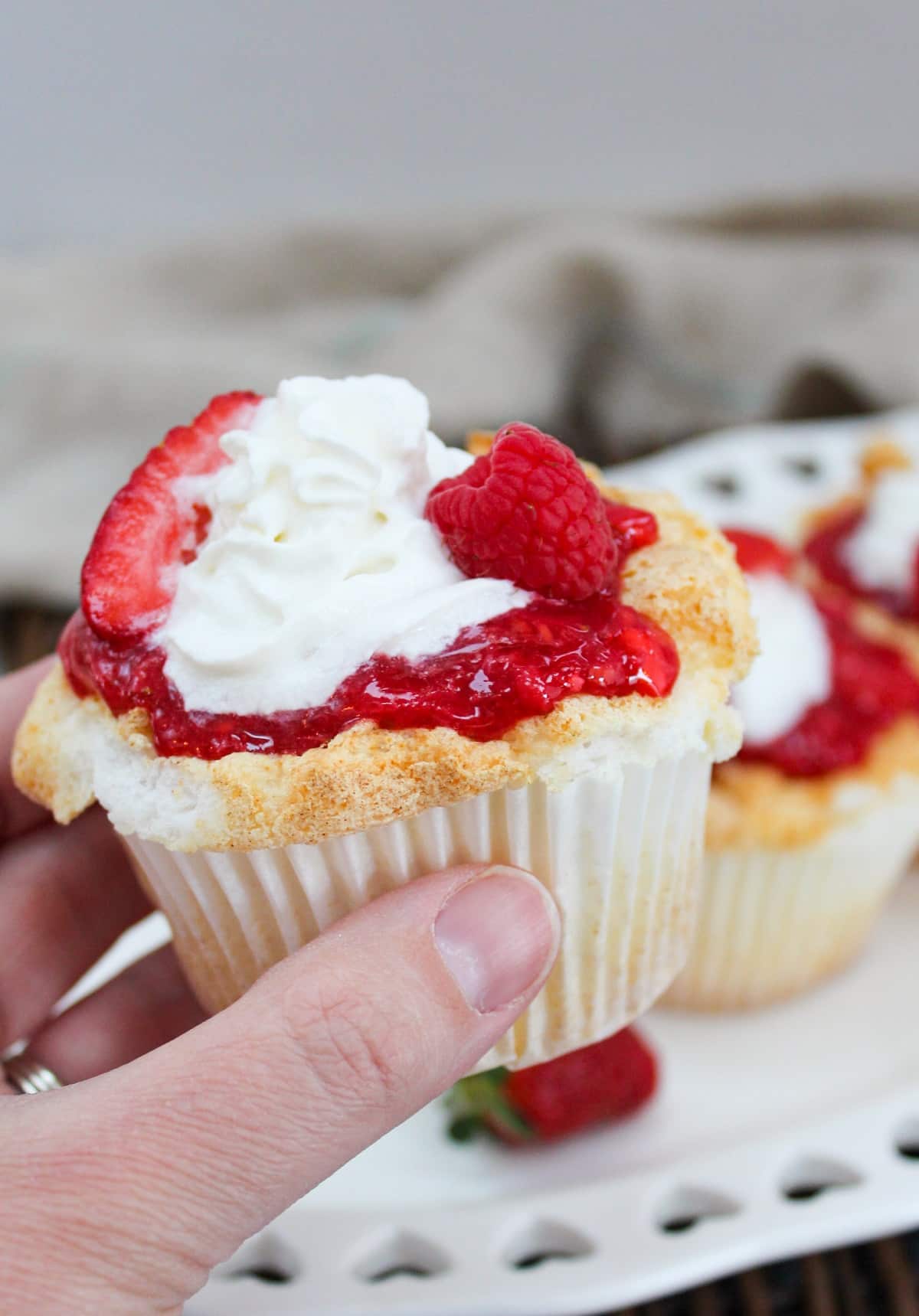 cupcake with berries and whipped cream on top held in hand.