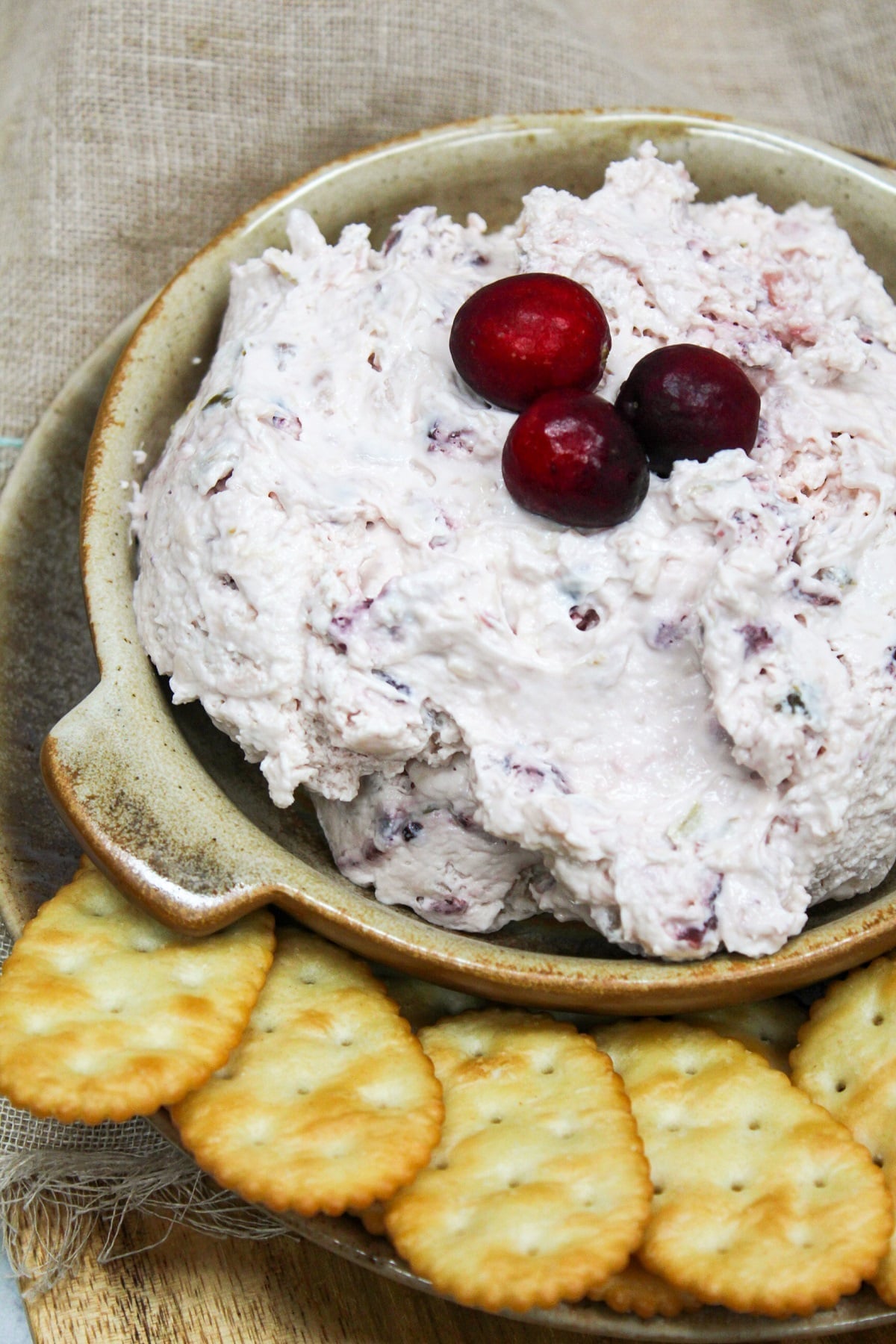 pink cranberry jalapeno dip topped with fresh cranberries on a bowl. Crackers are served on the side of the bowl.