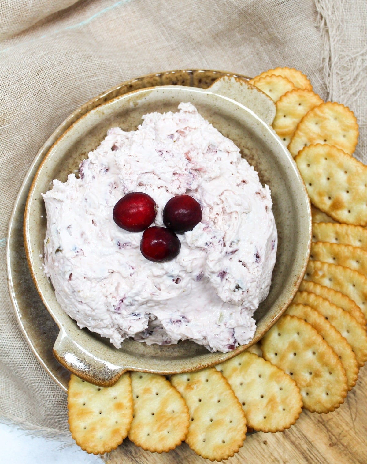 pink cranberry jalapeno dip topped with fresh cranberries on a bowl. Crackers are served on the side of the bowl.